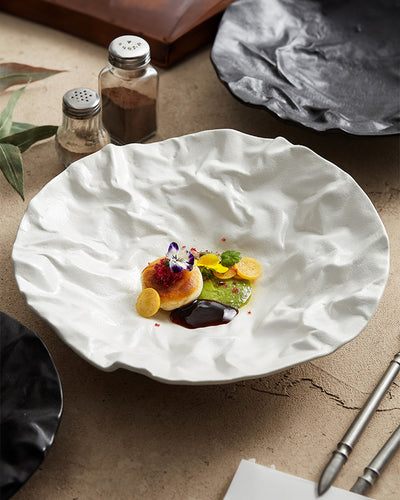 A deep plate with a moon crater design made of porcelain and ceramic. Luxury dining experience for restaurants, caterings and chef supplies