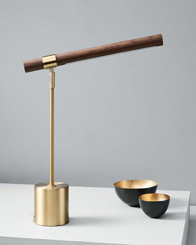 A desk lamp made of gold and wood next to two golden bowls on a white table