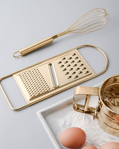 Golden egg beater made of stainless steel next to other golden kitchen utensils