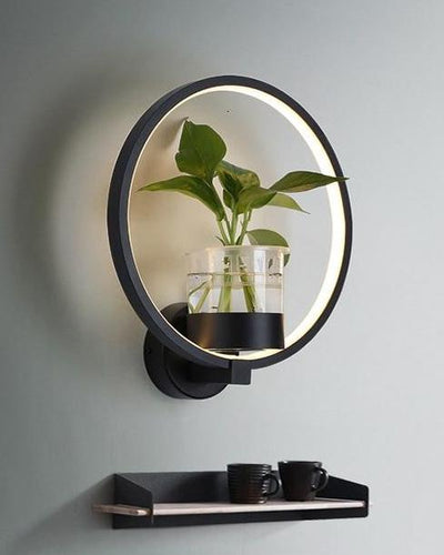 A black wall lamp, with a ring light shape and a plant in the middle on white background